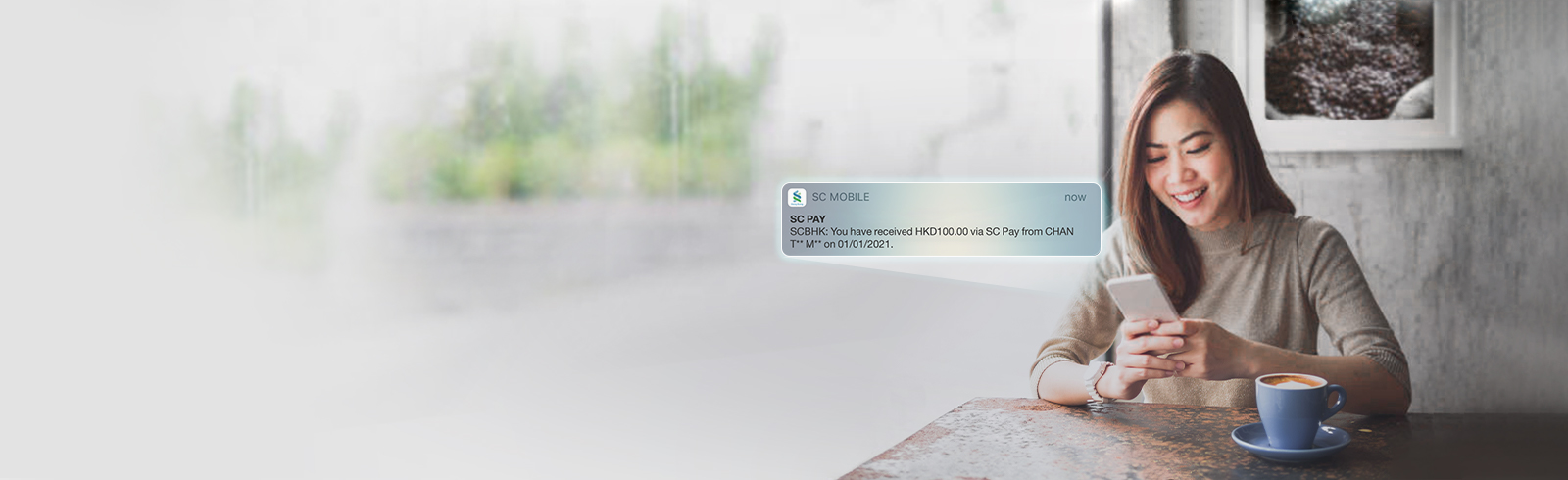 young lady using mobile in a cafe, receiving SC Pay push notification