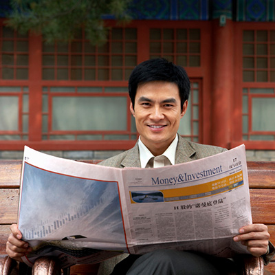 a man holding a financial news paper sitting on a bench