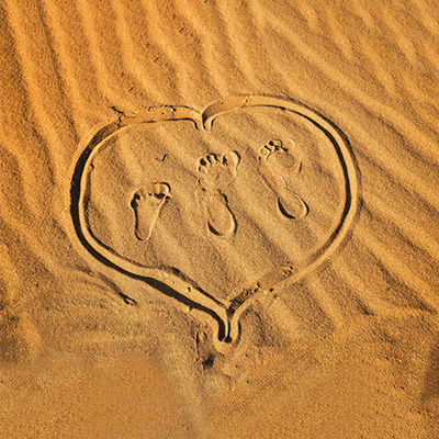 a heart shape with 2 adults and 1 kid's footprint on the sand