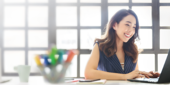 一名棕色頭髮穿着藍色背心外套的女士正在微笑地使用她的手提電腦